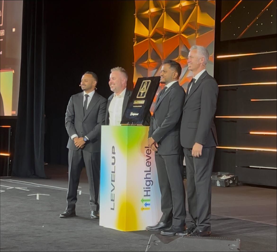 Jonathan Ferrell on stage at a HighLevel Level Up event, standing with three others beside an award plaque on a LEVELUP podium.