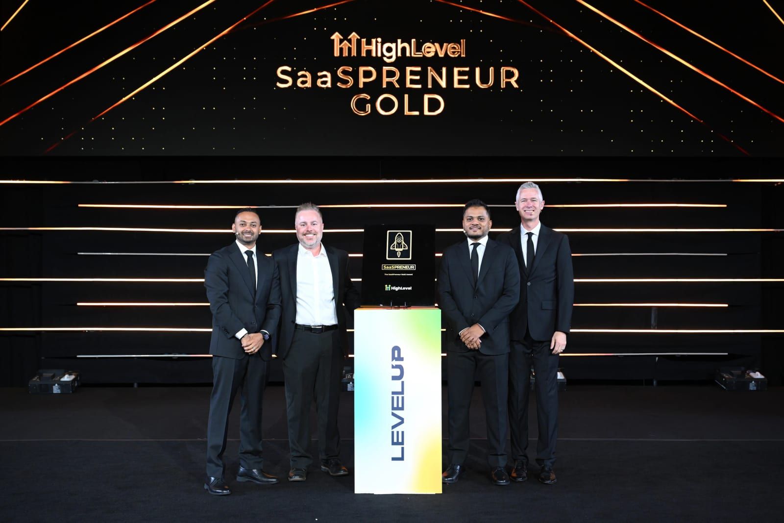 Jonathan, second from left, on the HighLevel LEVELUP stage receiving the SaaSPRENEUR Gold award with three others, the award trophy on a stand between them.